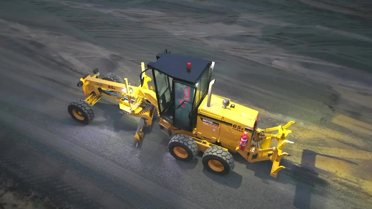 Grader trimming the pad under lights during the early shift
