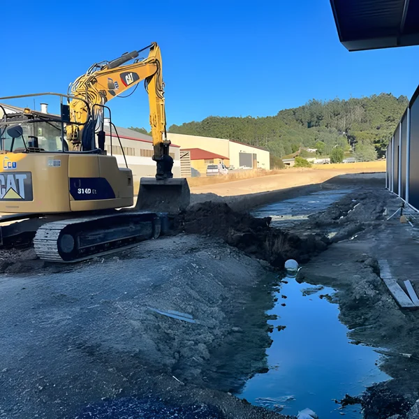 CAT 314D excavator cutting a drainage trench beside a commercial shed